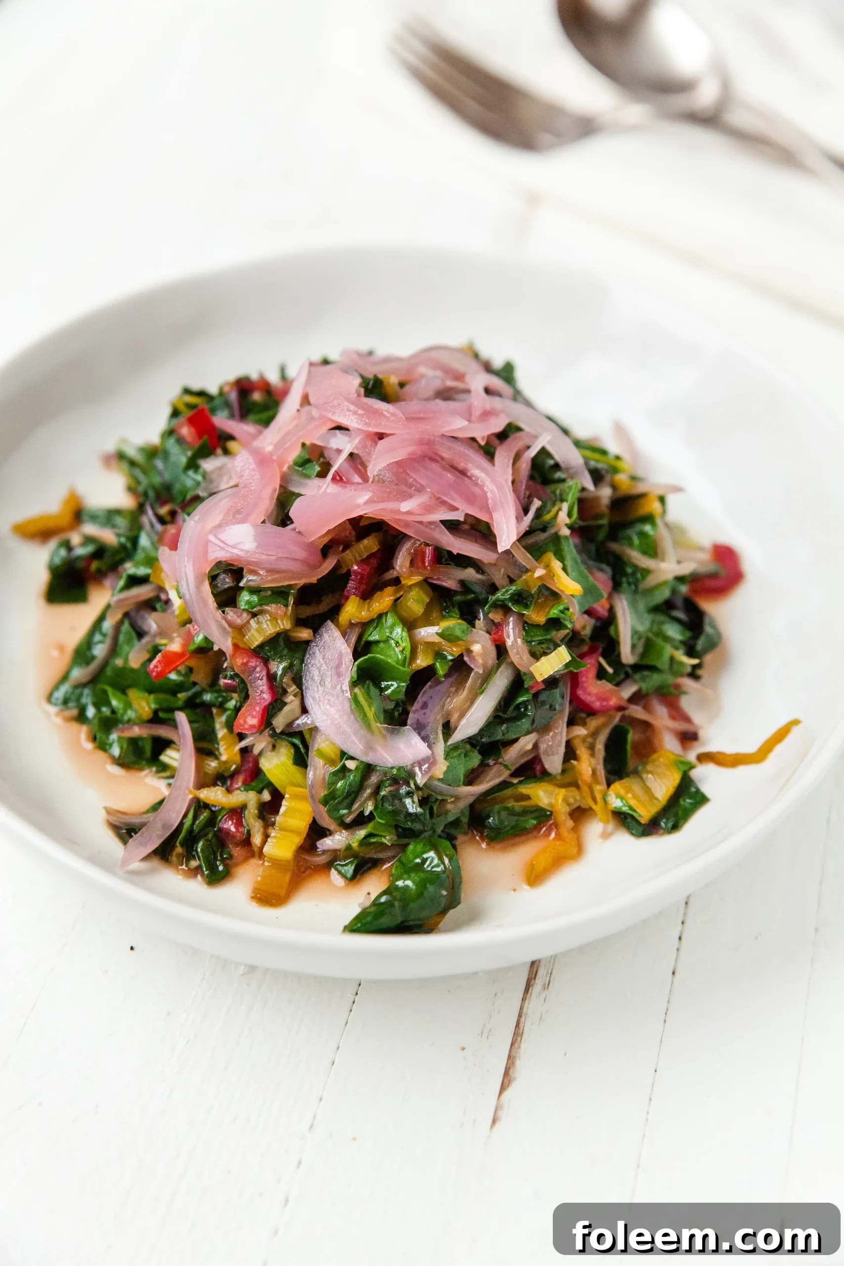 Sautéed Swiss Chardin white bowl with picked red onions.