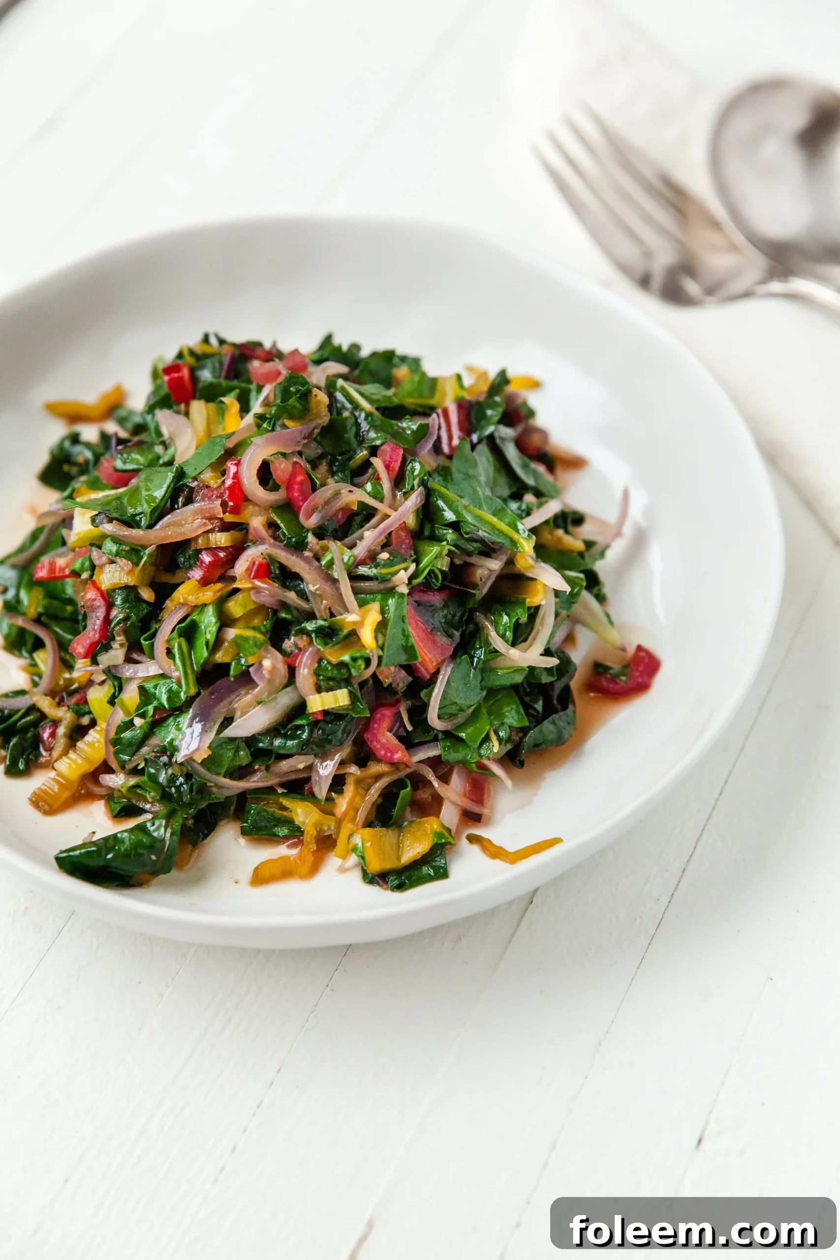 Sautéed Swiss Chard on white plate with fork and spoon.