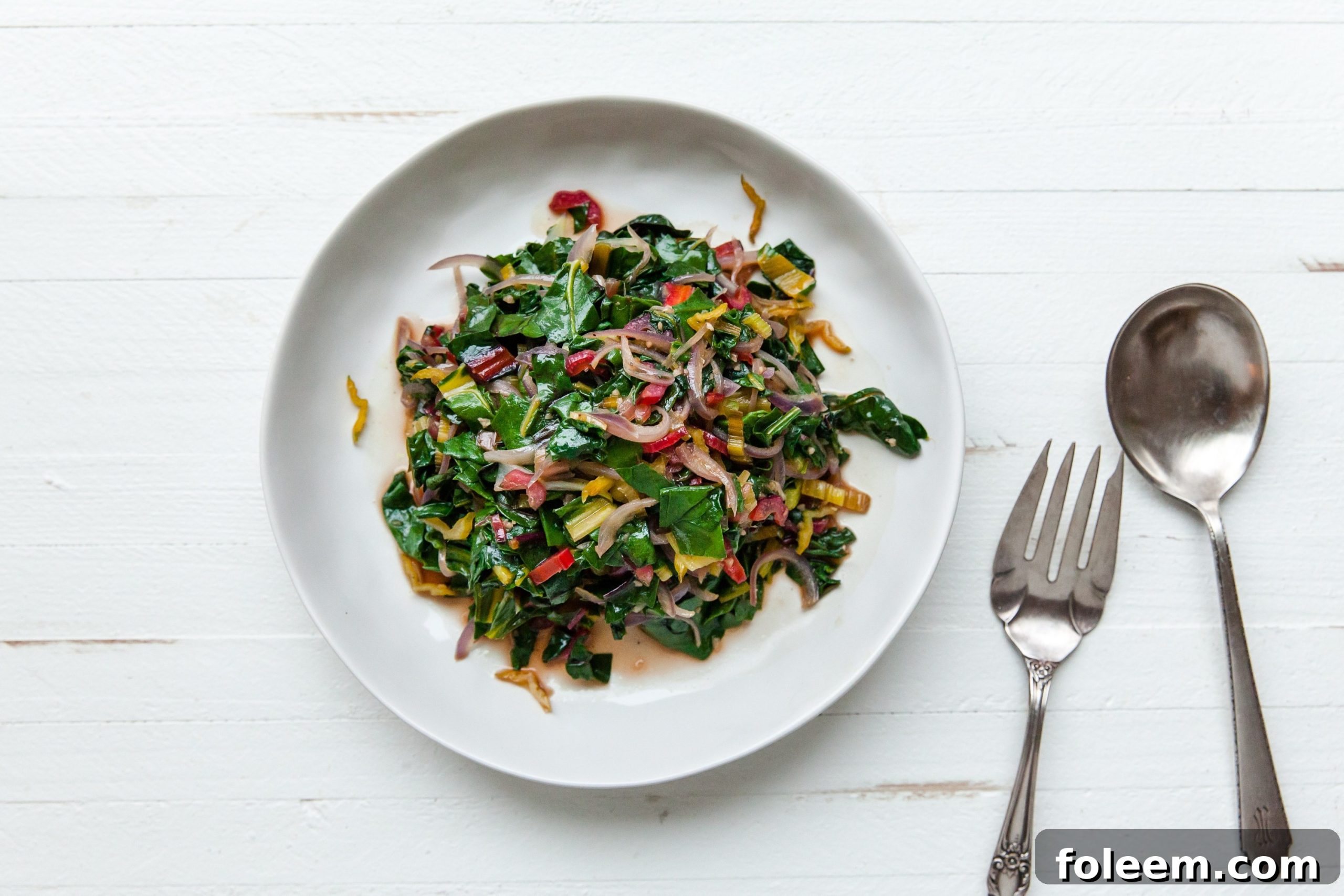 White bowl with Sautéed Swiss Chard next to fork and spoon.