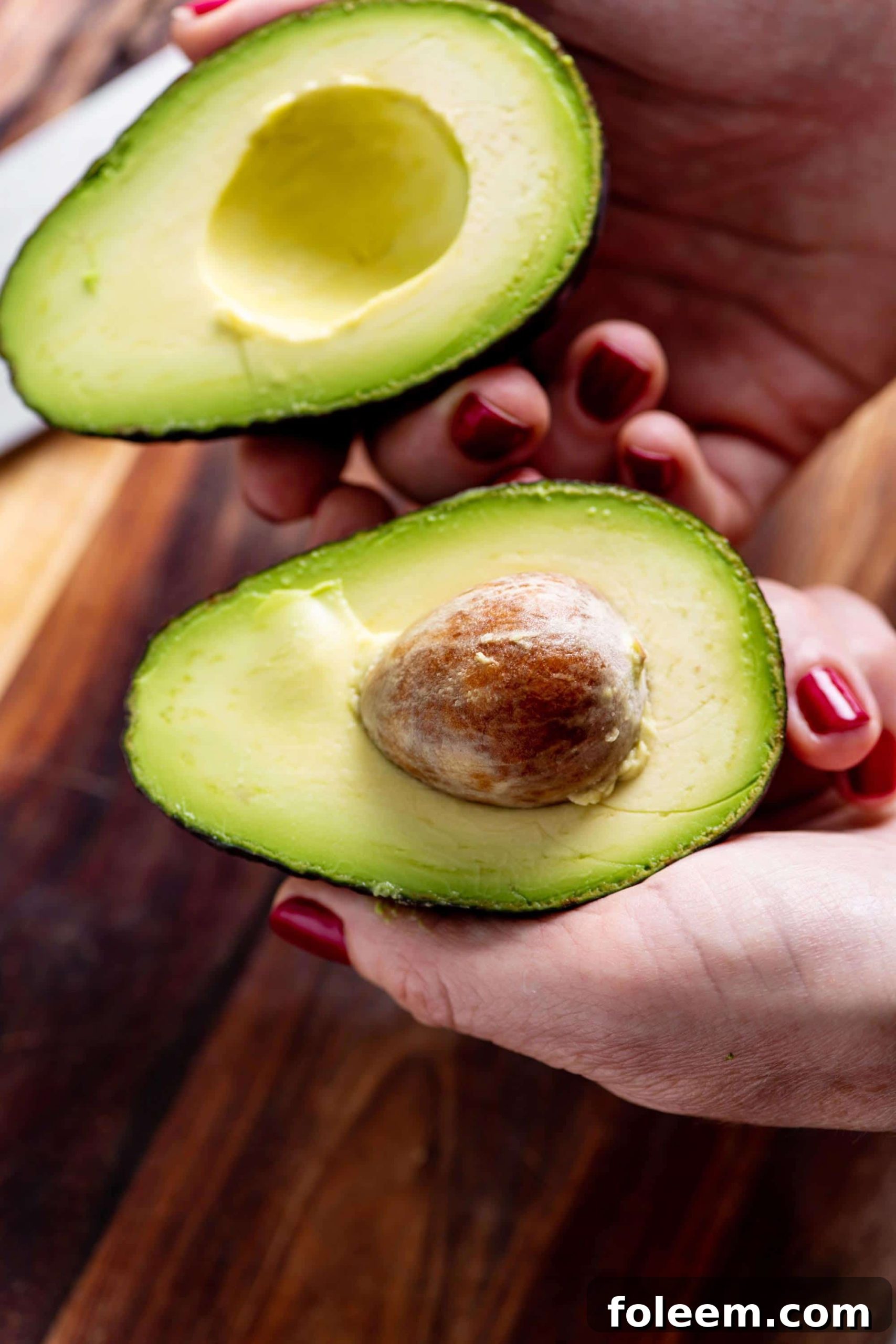 Woman holding avocado cut in half.