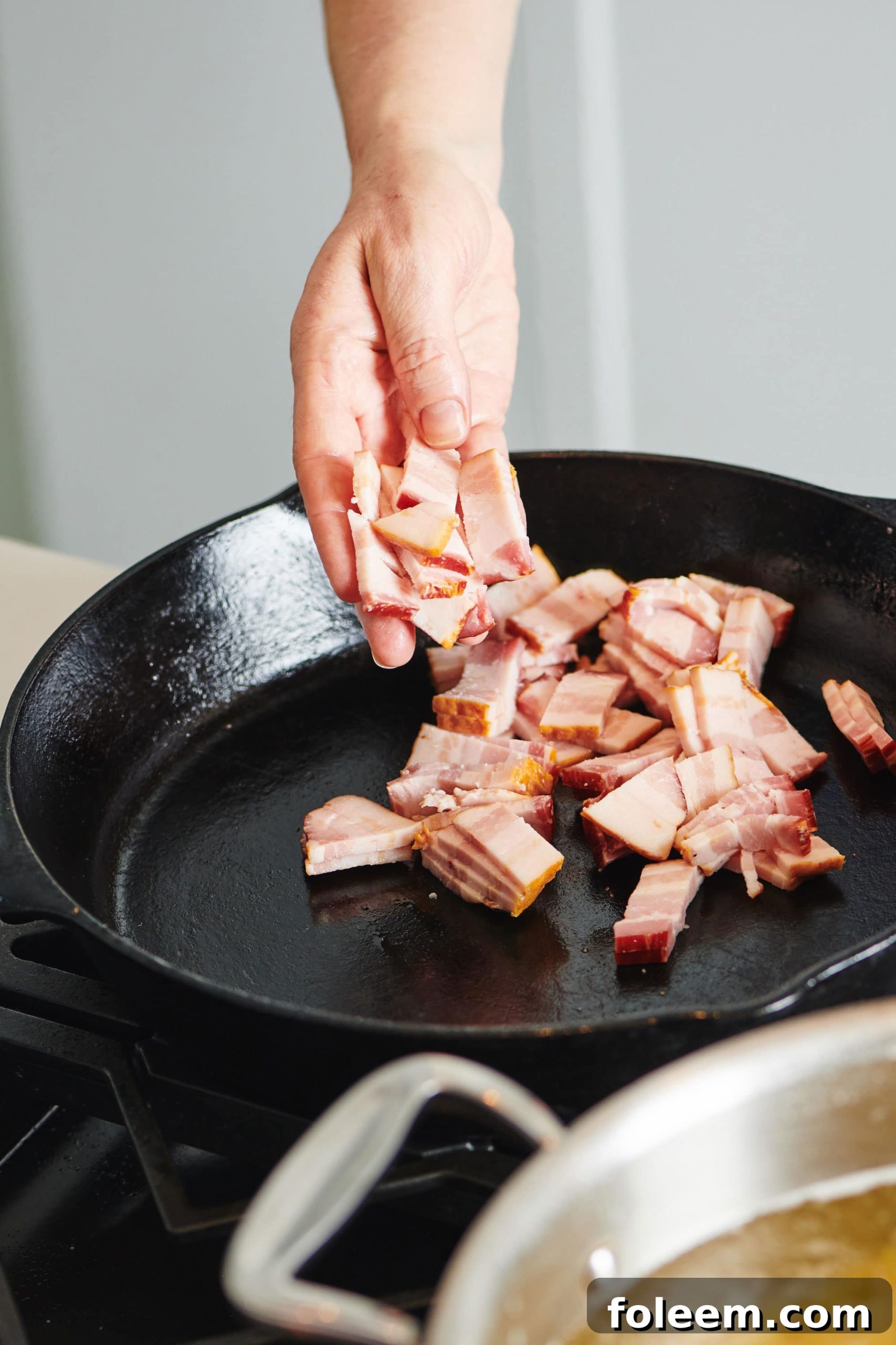 Woman putting uncooked sliced bacon into a cast iron pan.