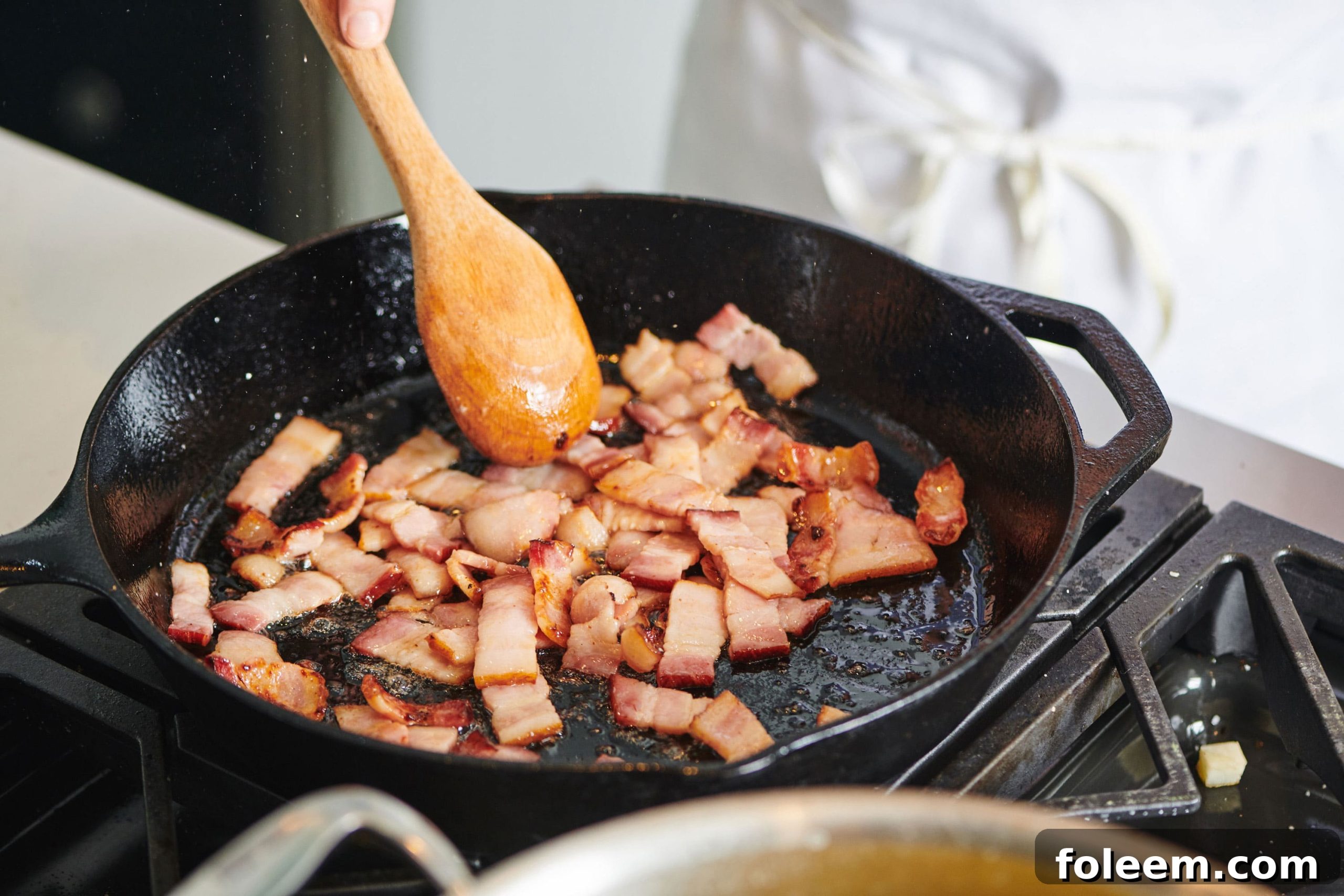 Spoon stirring Bacon Lardons in a cast iron pan.