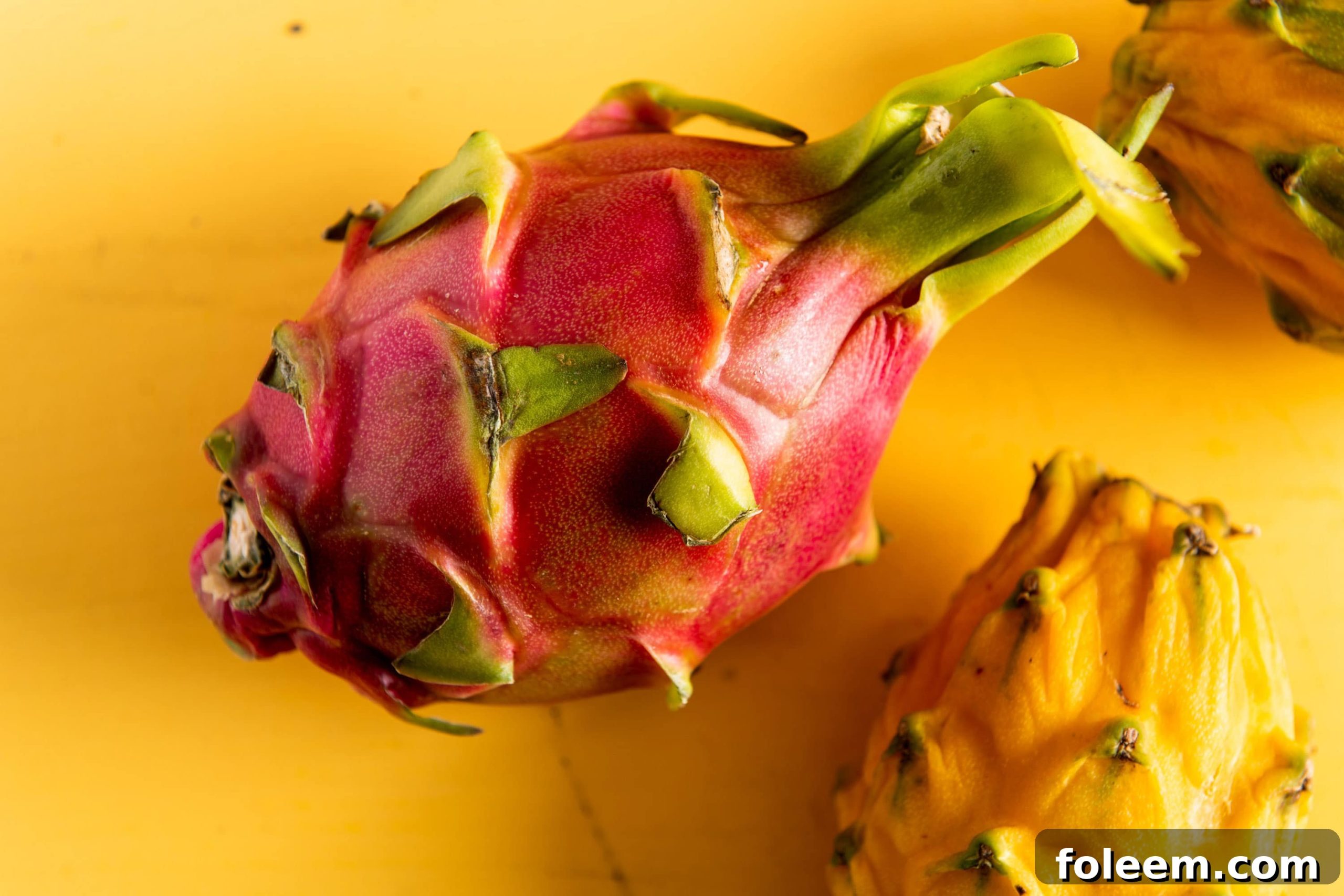 Pink uncut dragonfruit on yellow surface with yellow dragon fruit nearby.