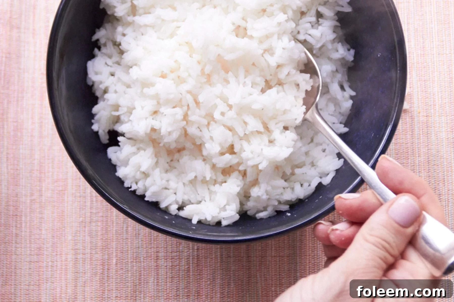 Katie Workman fluffing rice in bowl with fork.