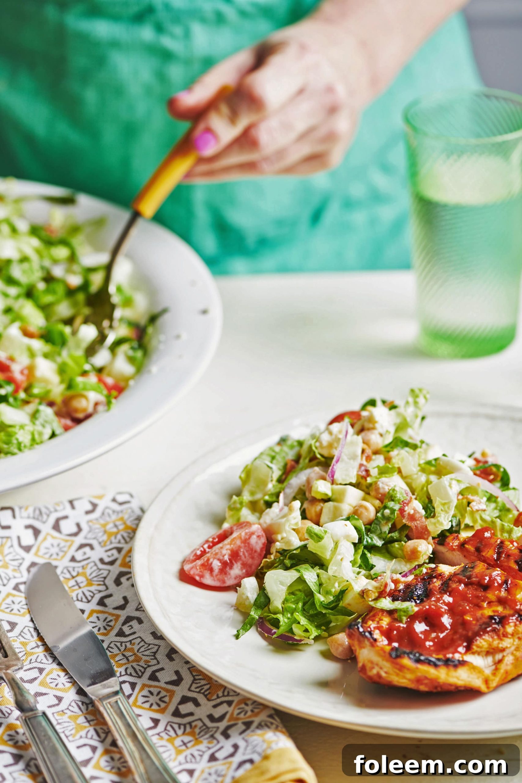 Woman in teal apron serving fresh salad onto a white plate.