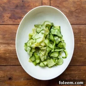 White serving plate of Zucchini Ribbon Salad on a wooden table.