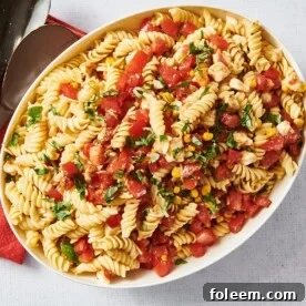 Serving bowl with Tomato Mozzarella Pasta Salad next to red napkin and silverware.