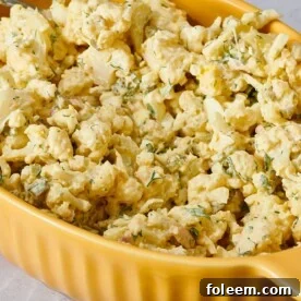 Cauliflower potato salad in yellow serving dish on table.