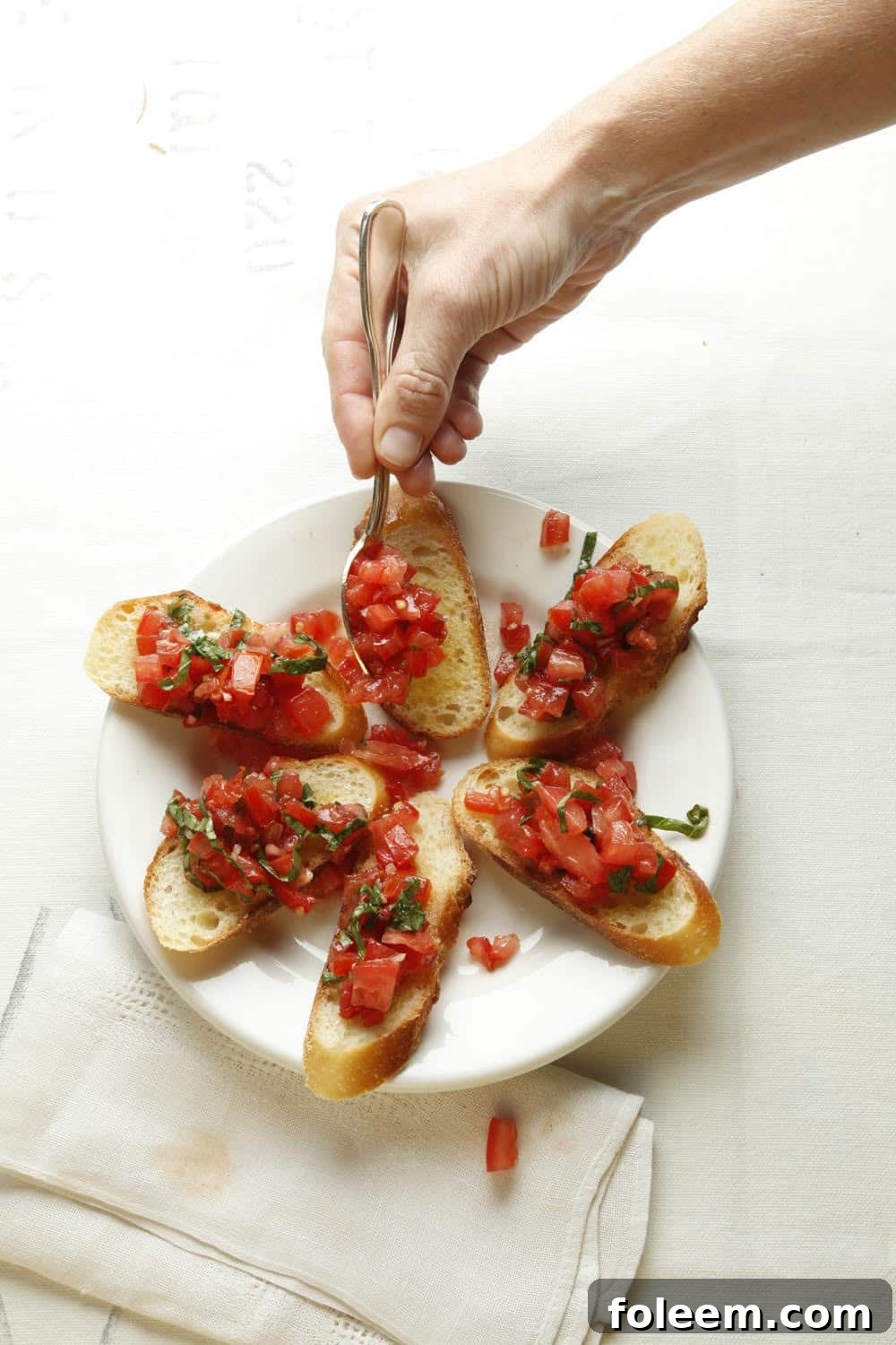 Woman spooning tomatoes onto bruschetta.