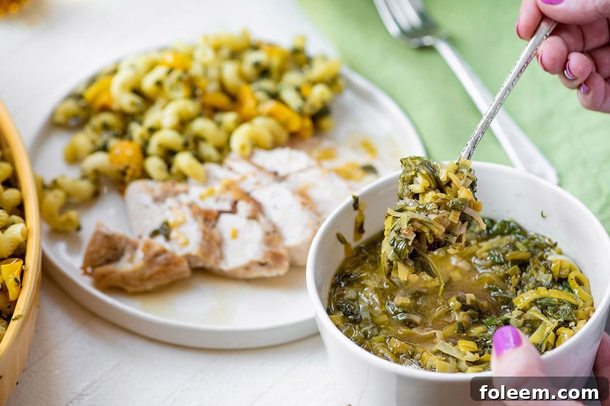 Serving white wine pan sauce with greens and leeks over sliced chicken.