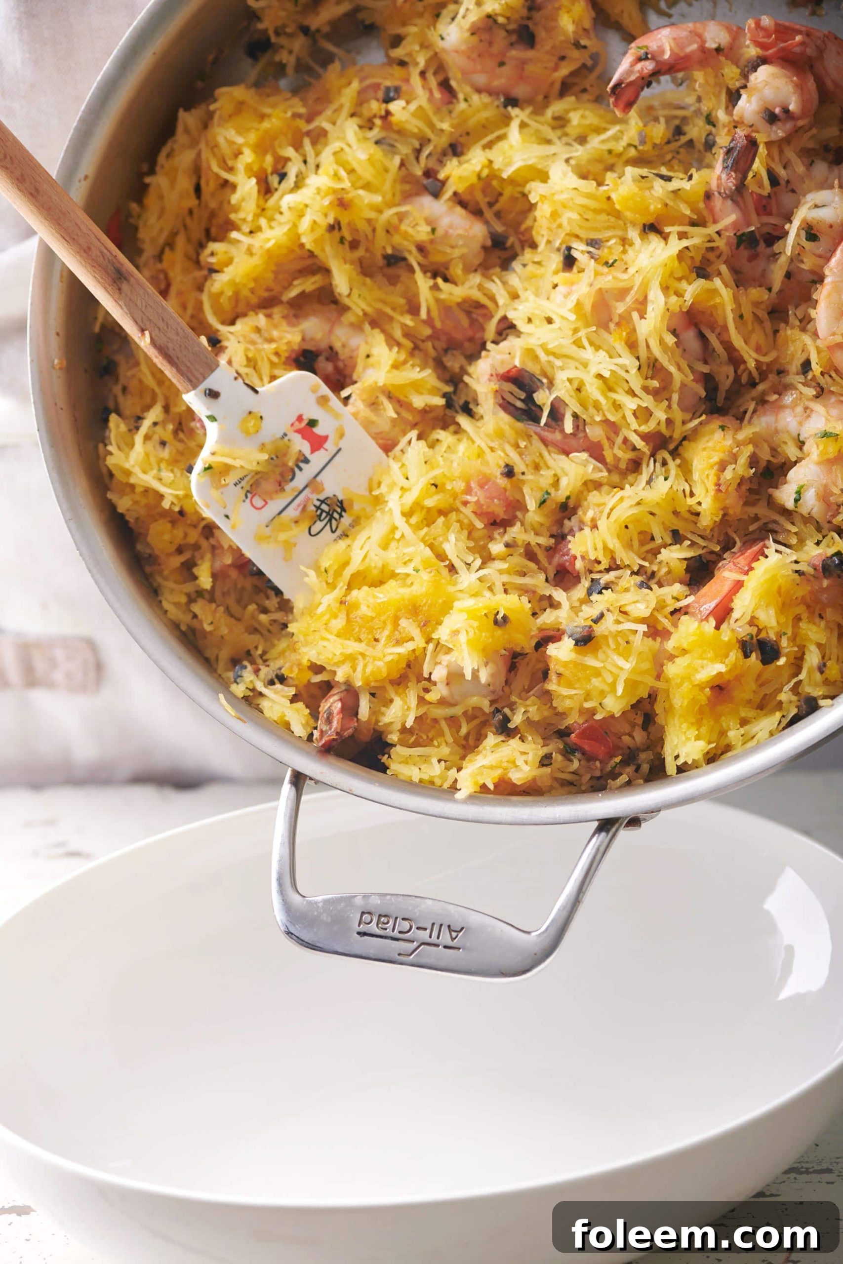 Spatula taking Greek-Style Spaghetti Squash with Shrimp from a skillet into a bowl.