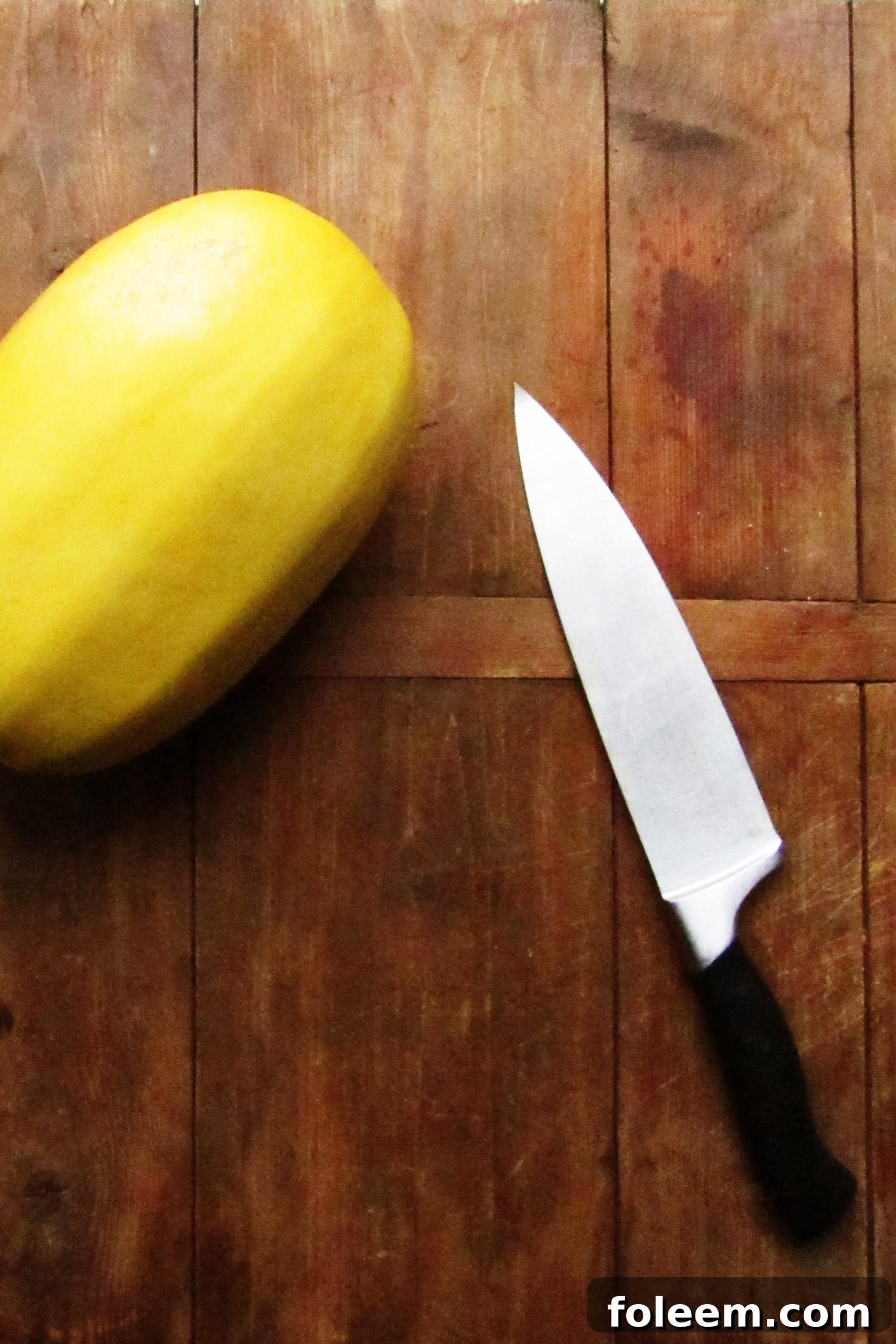 Whole spaghetti squash and a knife on a wooden board.