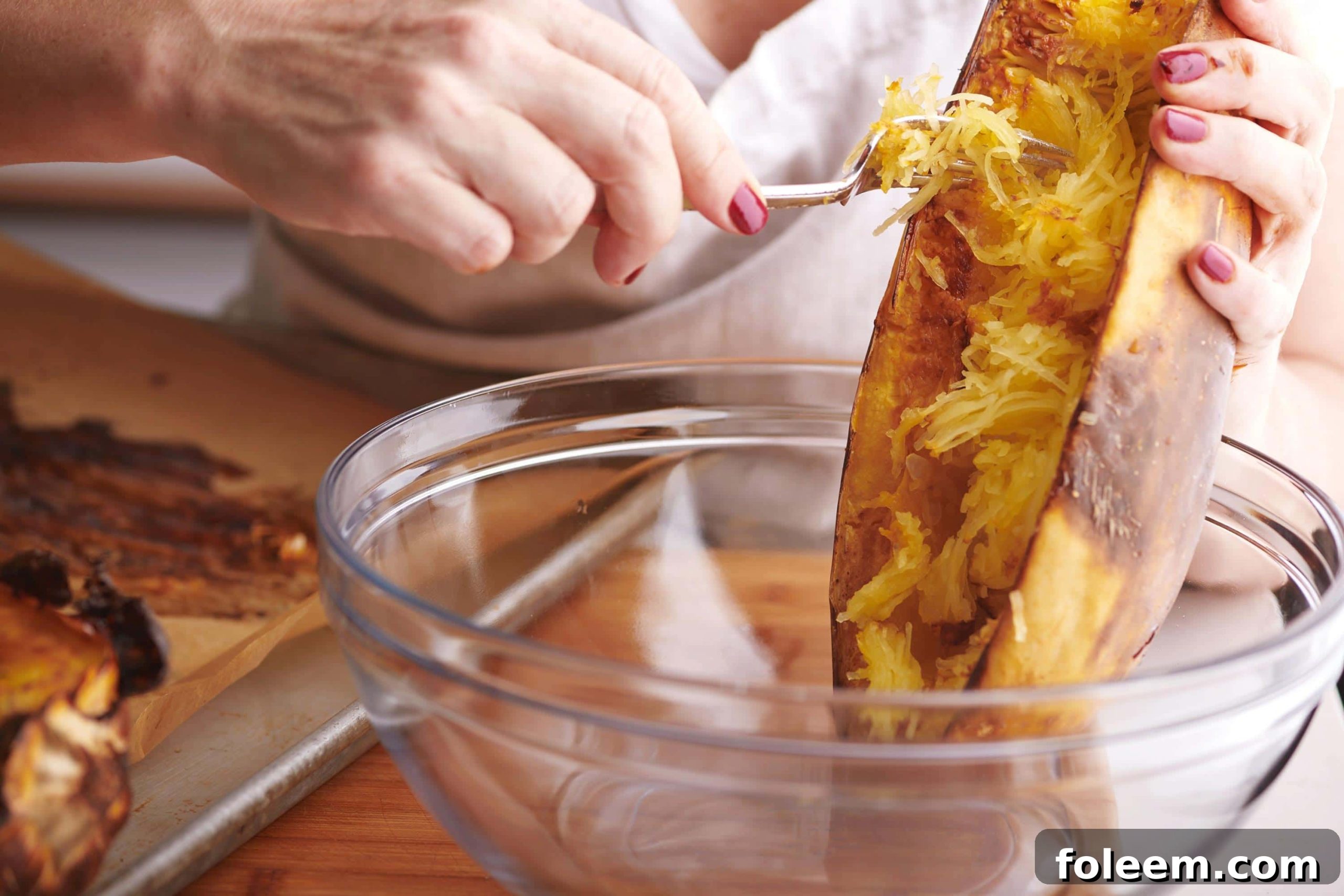 Woman scraping roasted spaghetti squash into bowl.