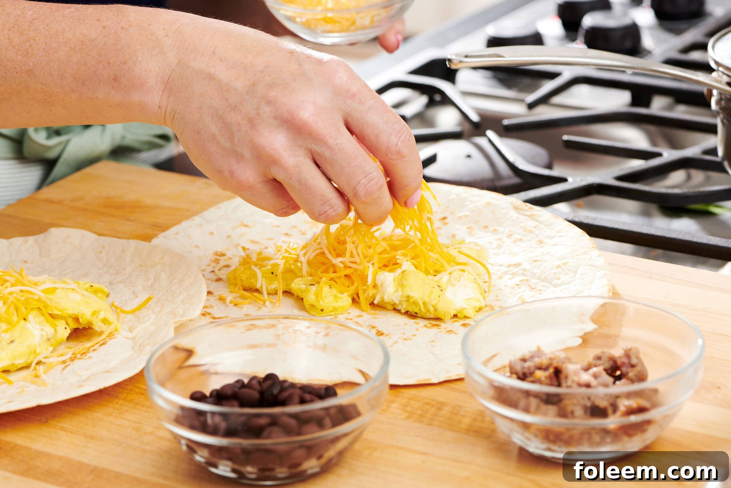 Woman placing shredded cheese onto eggs on a tortilla.