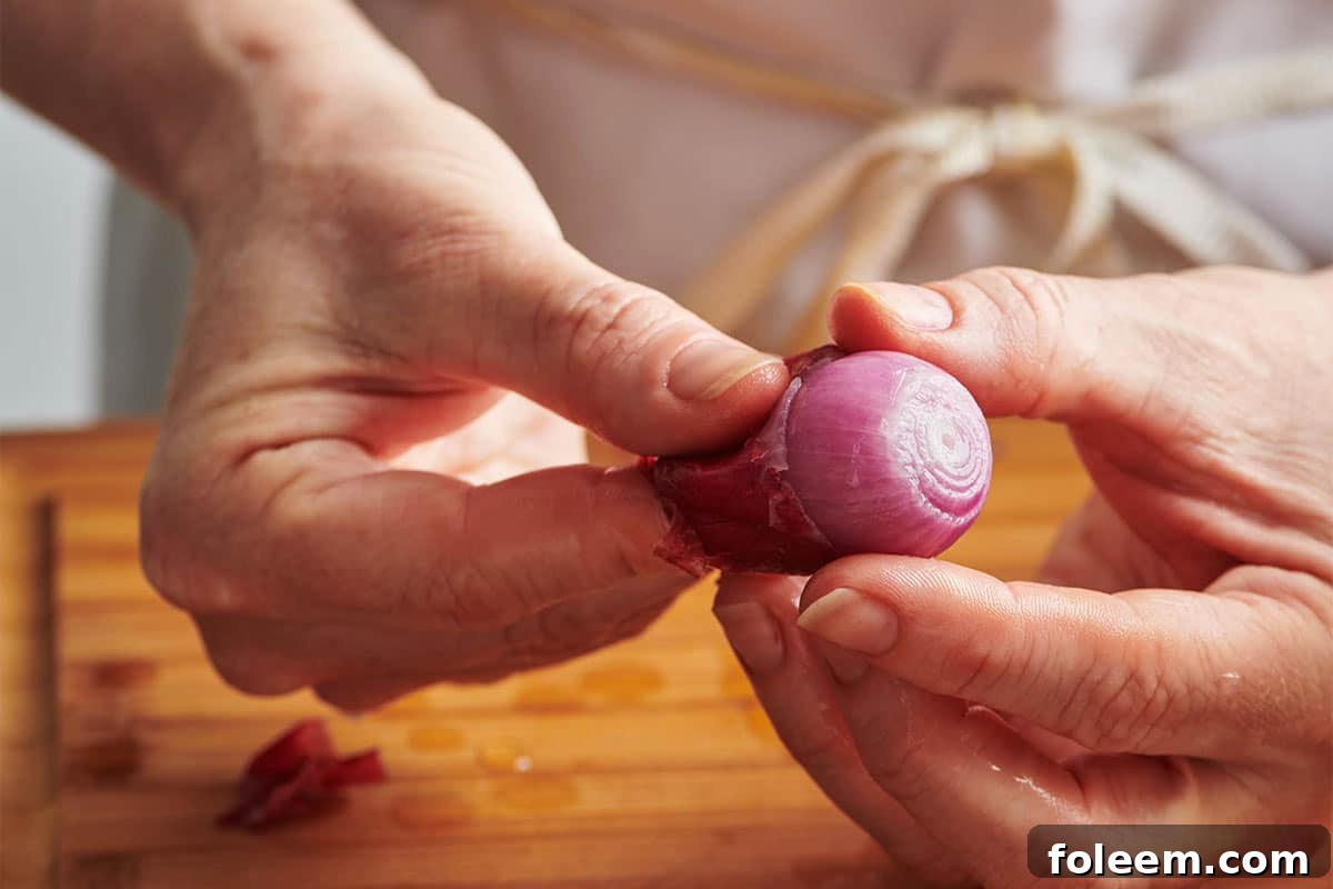 Woman sliding the peel off of a red pearl onion.