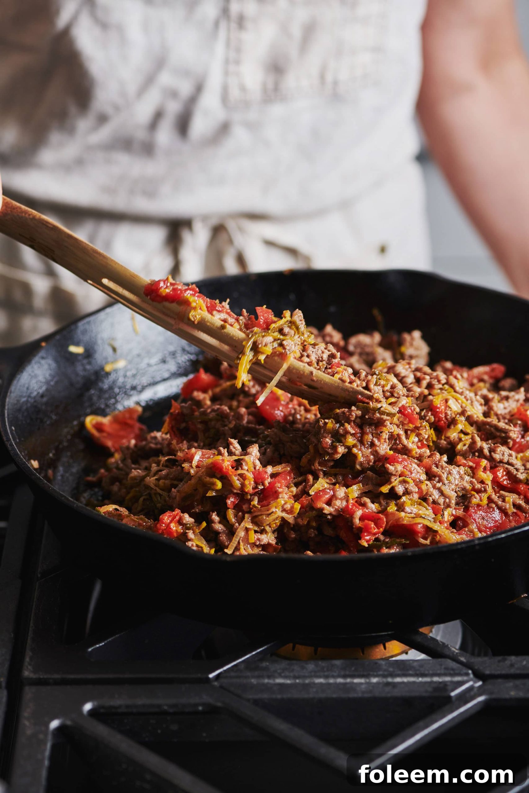 Woman stirring ground beef in cast-iron pan.