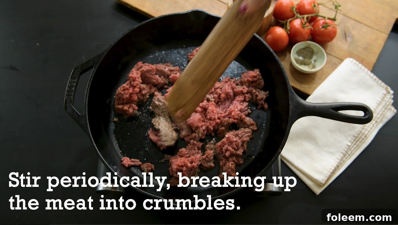 Breaking up ground beef into crumbles as it cooks in cast-iron pan.