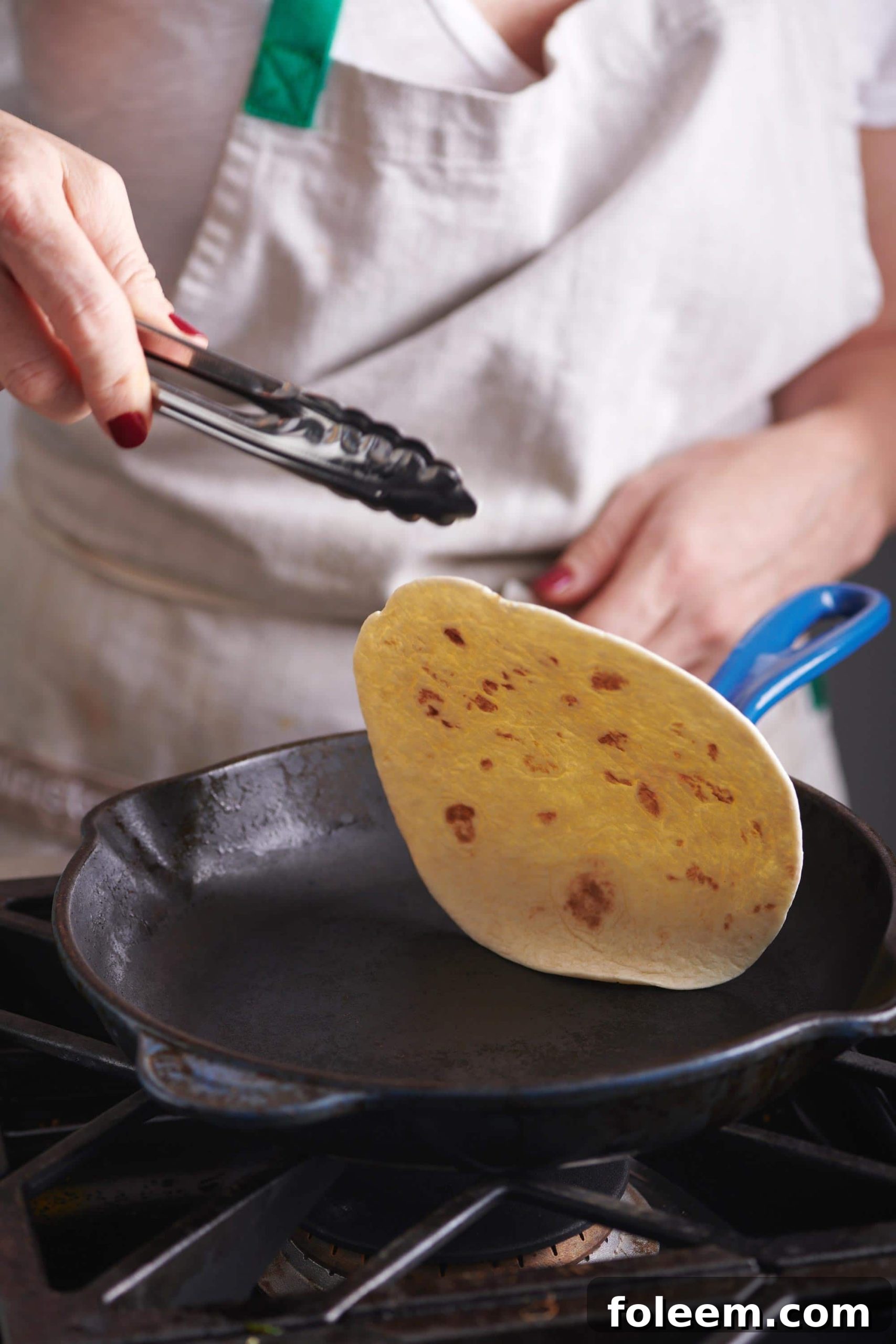 Woman flipping a tortilla in a skillet with tongs.