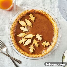 Homemade pumpkin pie with pastry leaf decorations on table.