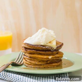 Green plate on table with pumpkin pie spice pancakes stacked high.