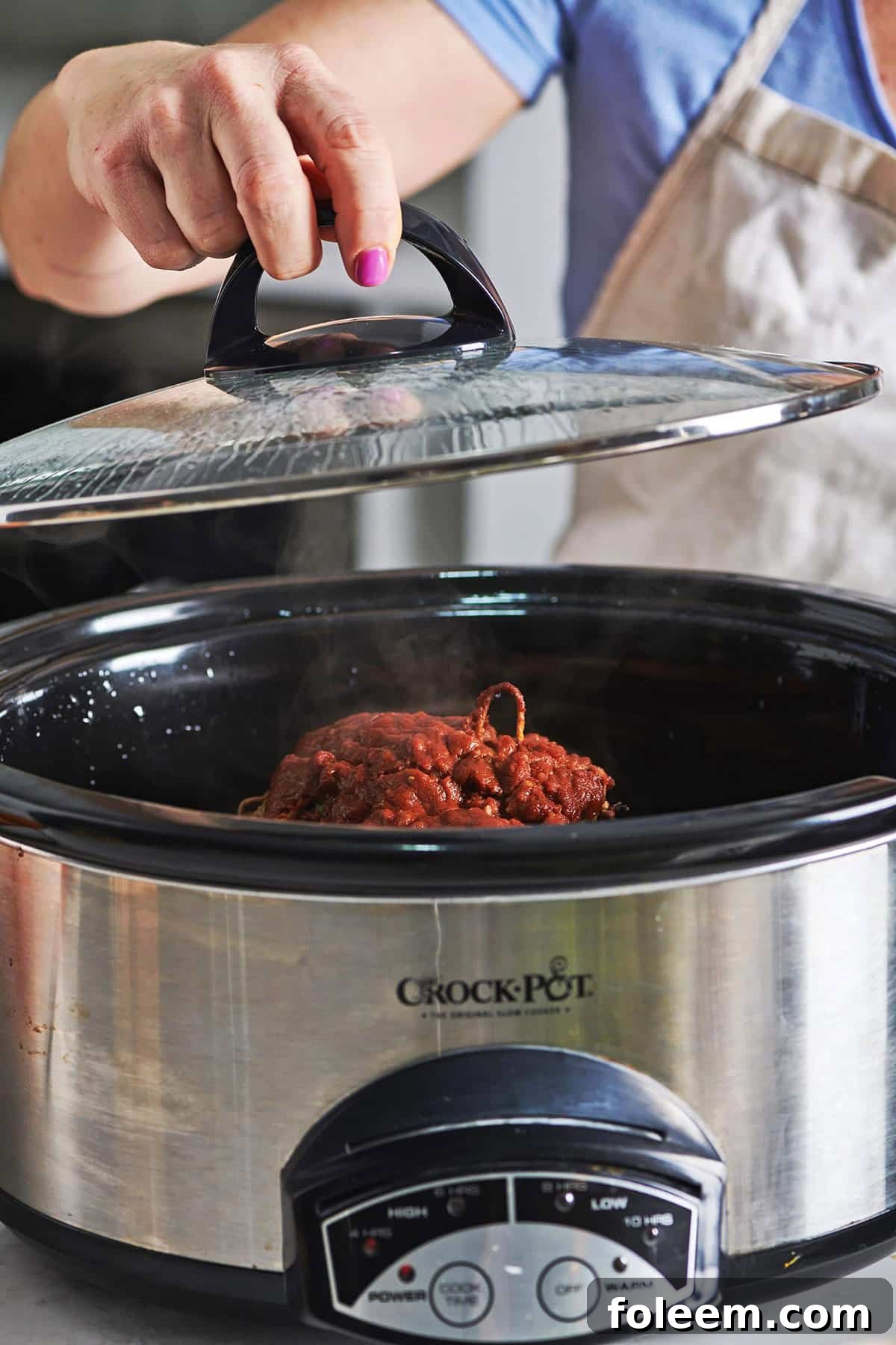 Woman lifting crockpot lid up with BBQ lamb in the pot.