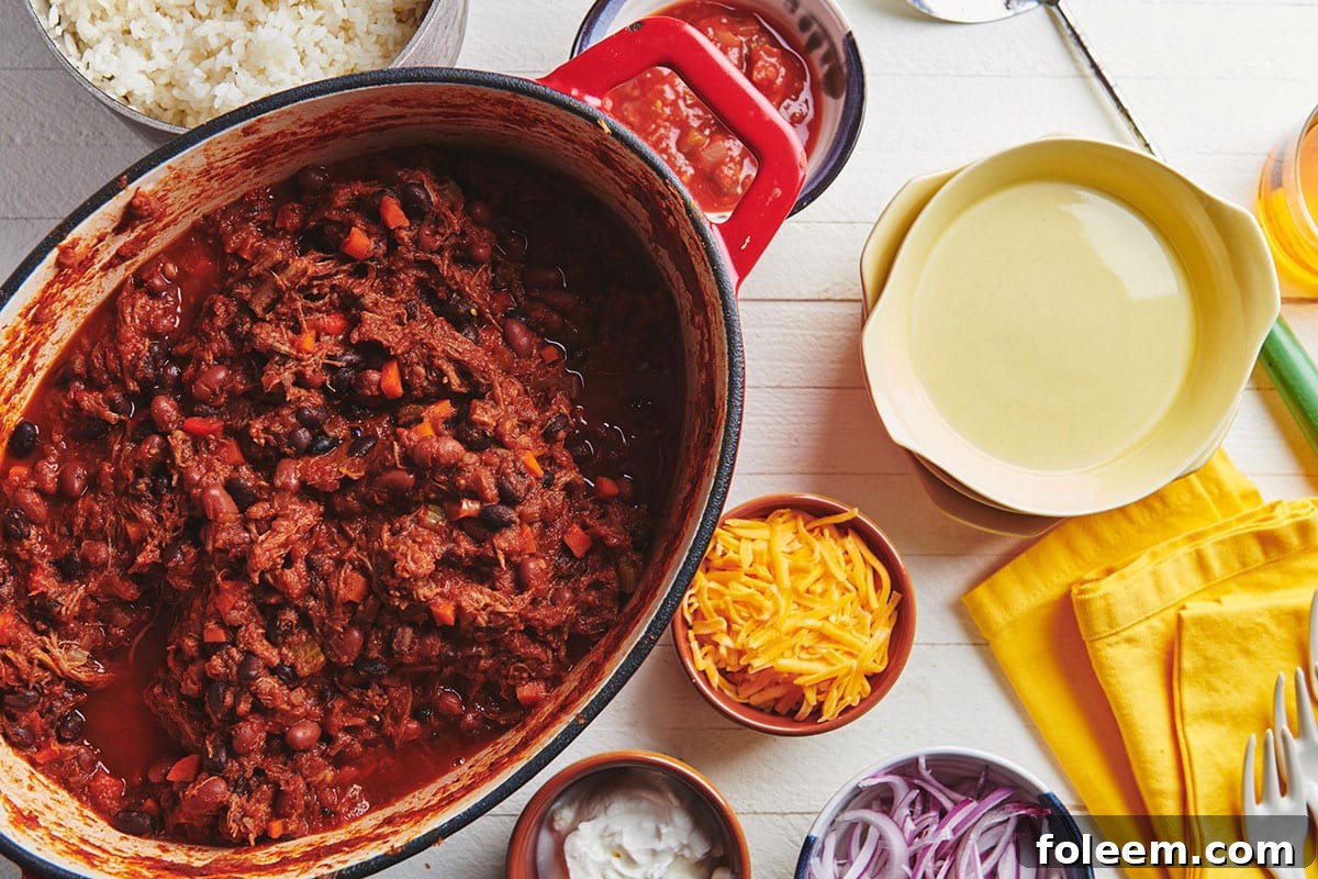 Barbacoa Beef Chili in pot on table with toppings in bowls.