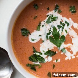 Creamy tomato soup in bowl with spoon on plate.