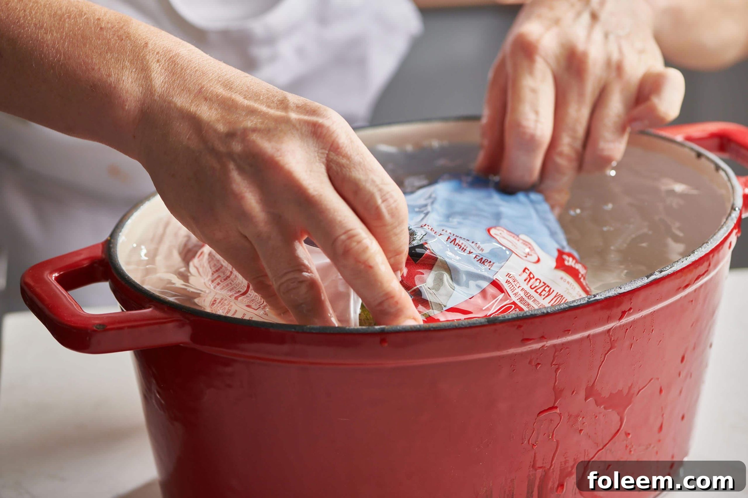 Woman putting a frozen, wrapped turkey into water.