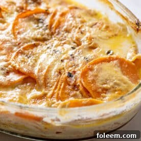 Creamy scalloped sweet potatoes in glass baking pan on table.