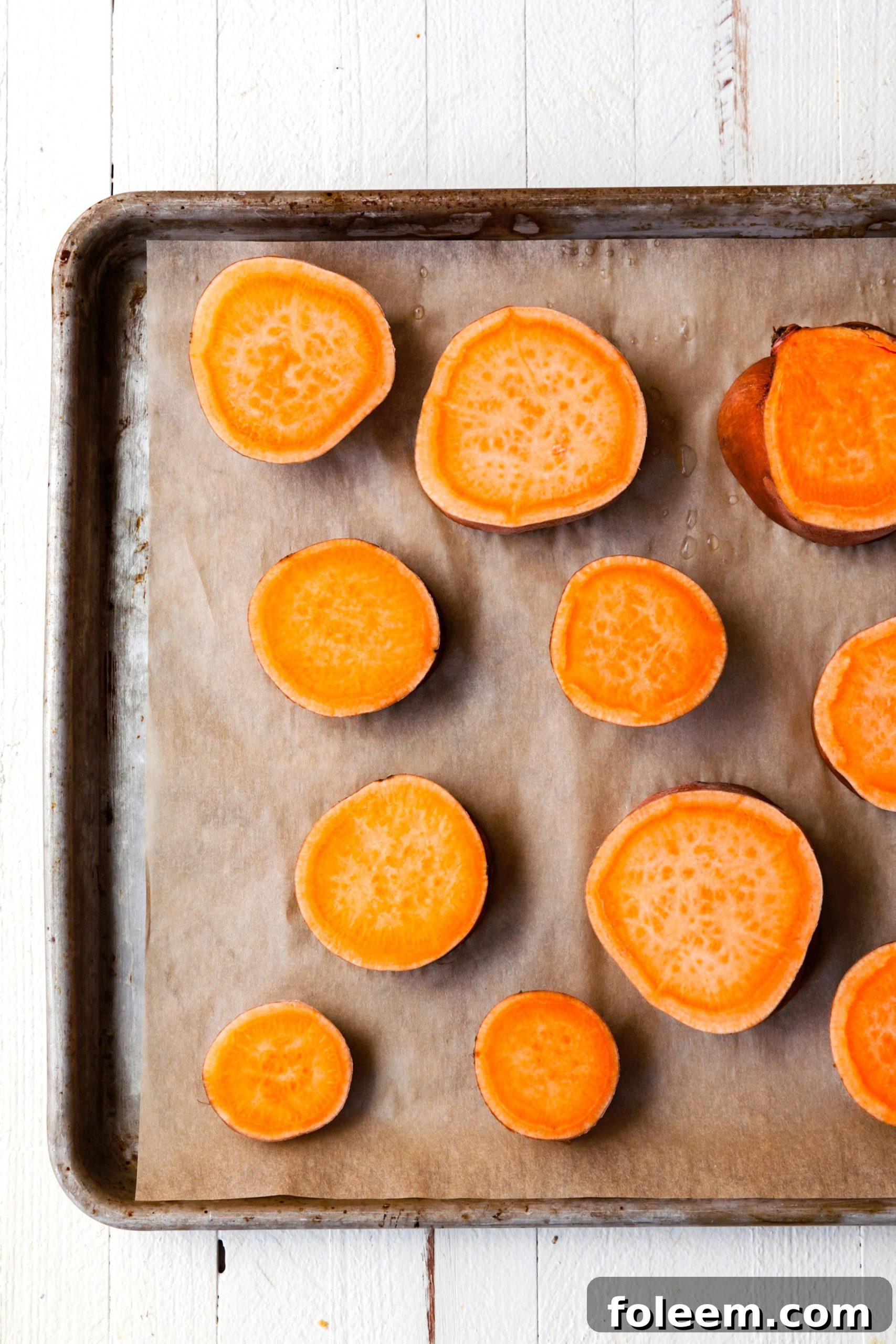 Slices of sweet potato on a parchment lined baking sheet.