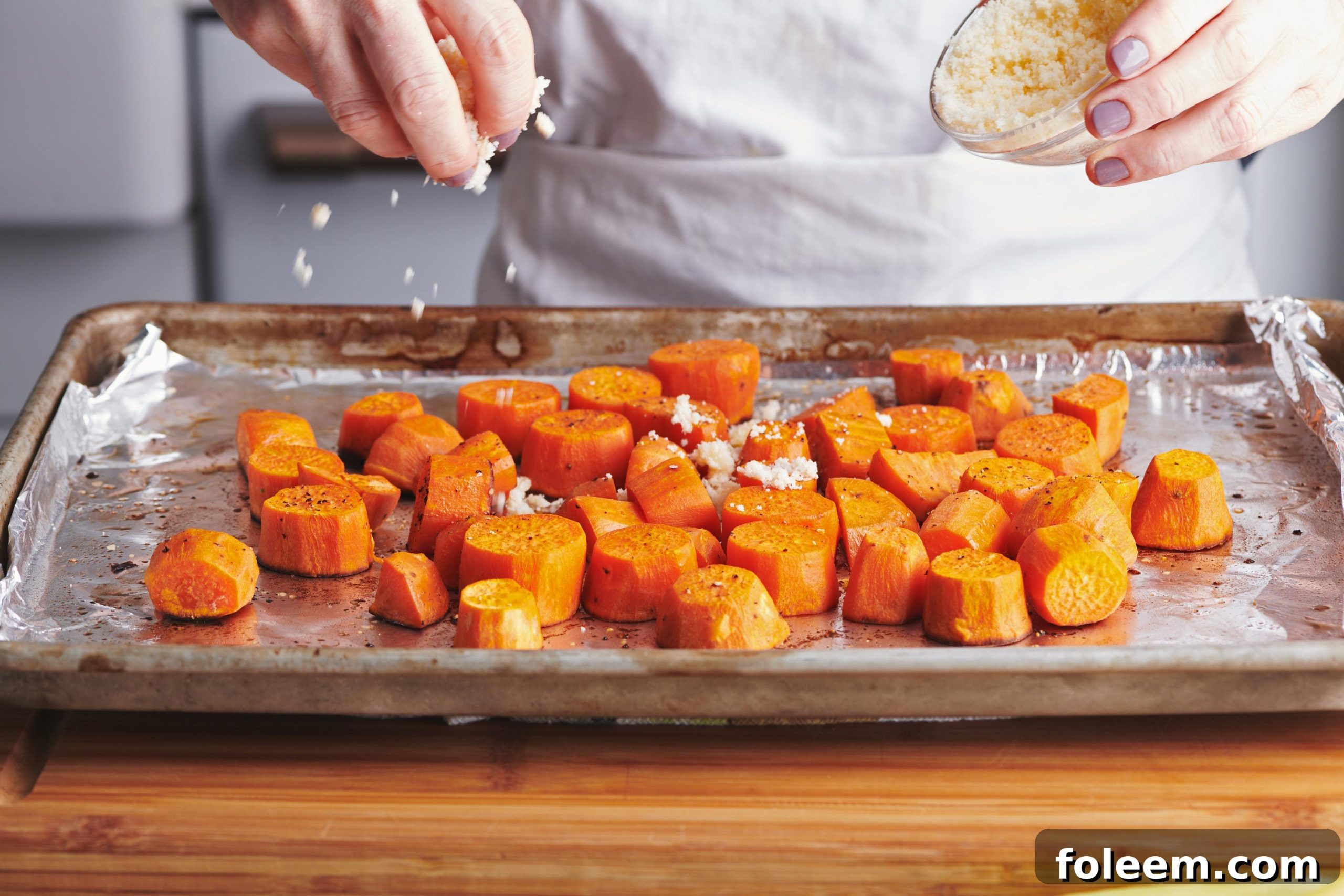 Woman seasoning Garlic-Parmesan Sweet Potatoes on a baking sheet.