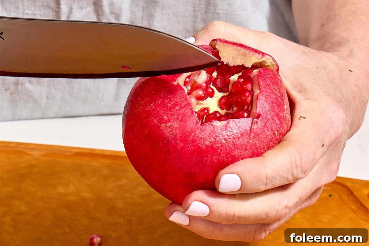 Woman slicing fresh pomegranate open with knife.