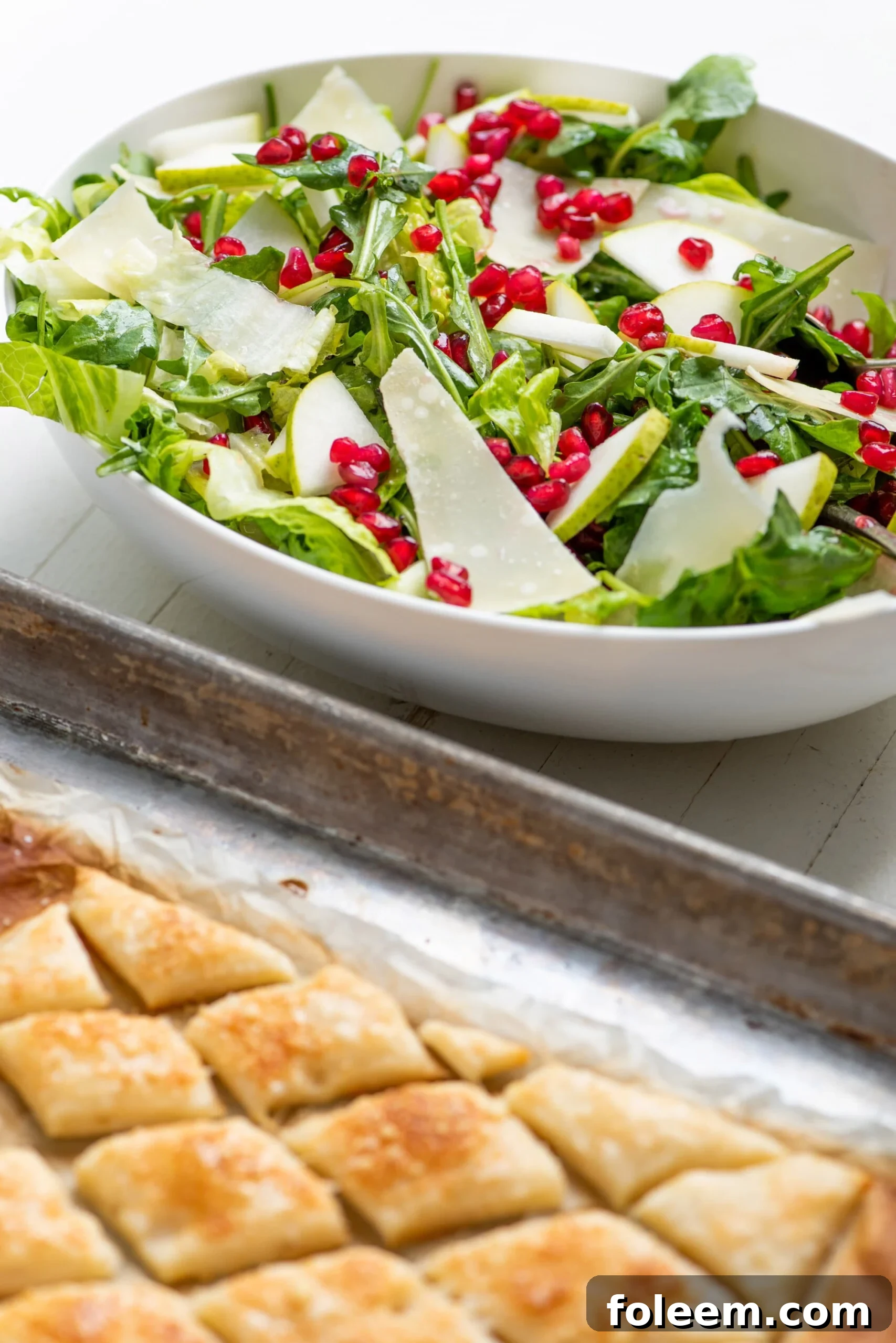 Green Salad with Pears, Parmesan and Pomegranate Seeds in white bowl with puff pastry.