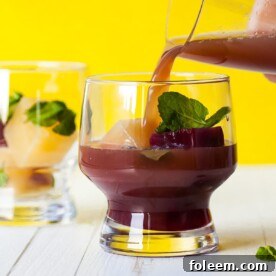 Pouring Pomegranate Orange Mocktail into glass with mint.