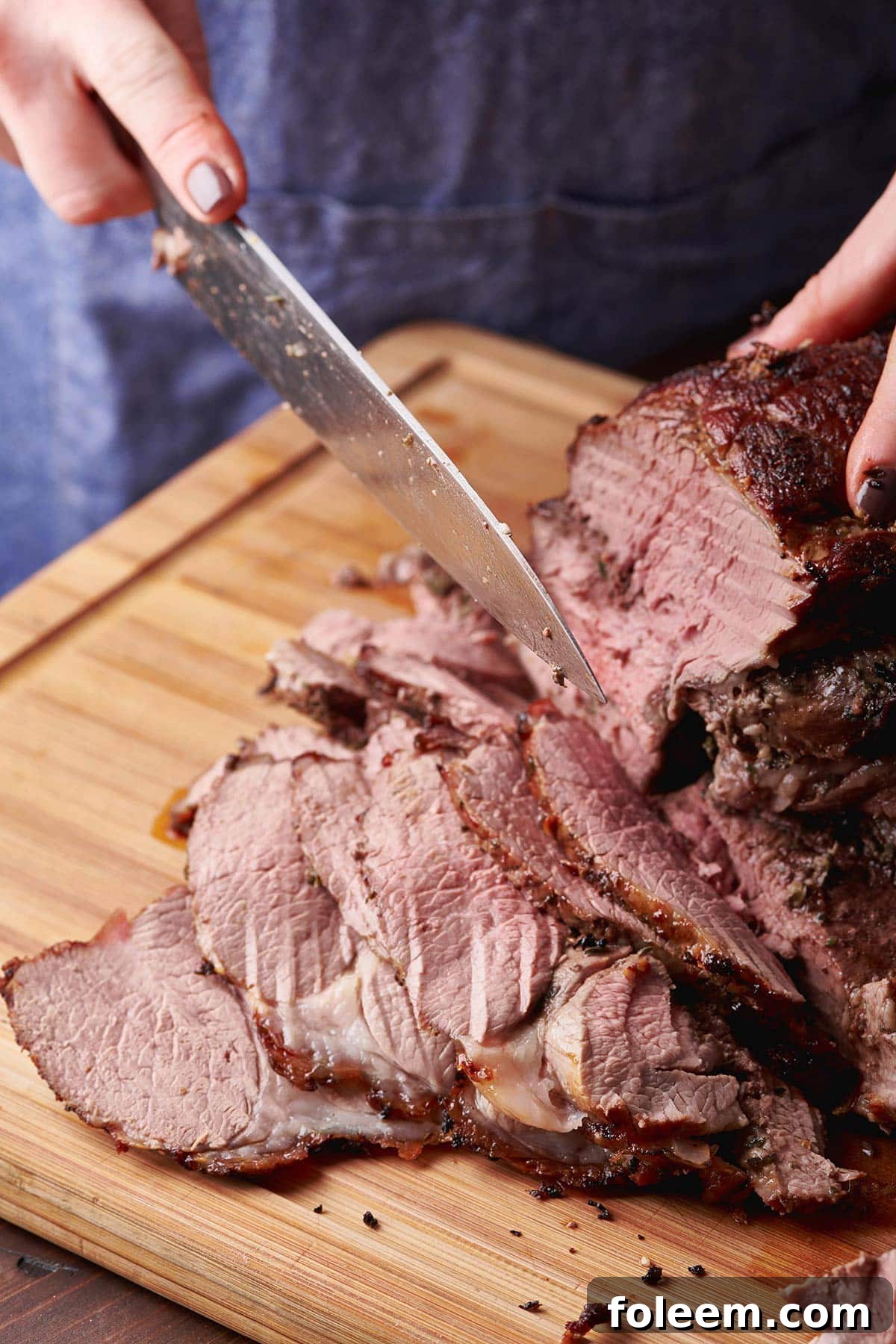 Woman slicing a Greek-Style Butterflied Leg of Lamb on a wooden cutting board.