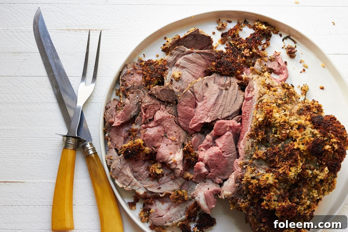 Partially sliced crusted leg of lamb on plate with fork and knife.