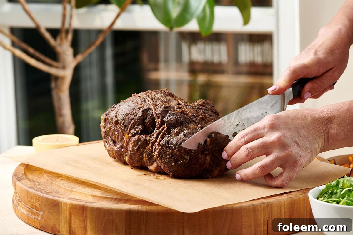 Slicing Slow Cooked Moroccan Leg of Lamb on cutting board with large knife.