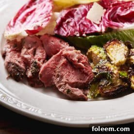 Greek-style leg of lamb slices on plate with salad and Brussels sprouts.