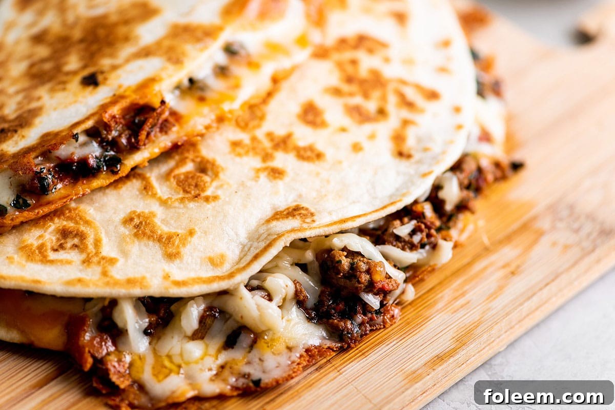 Cheesy Ground Beef Quesadillas stacked on wood cutting board.