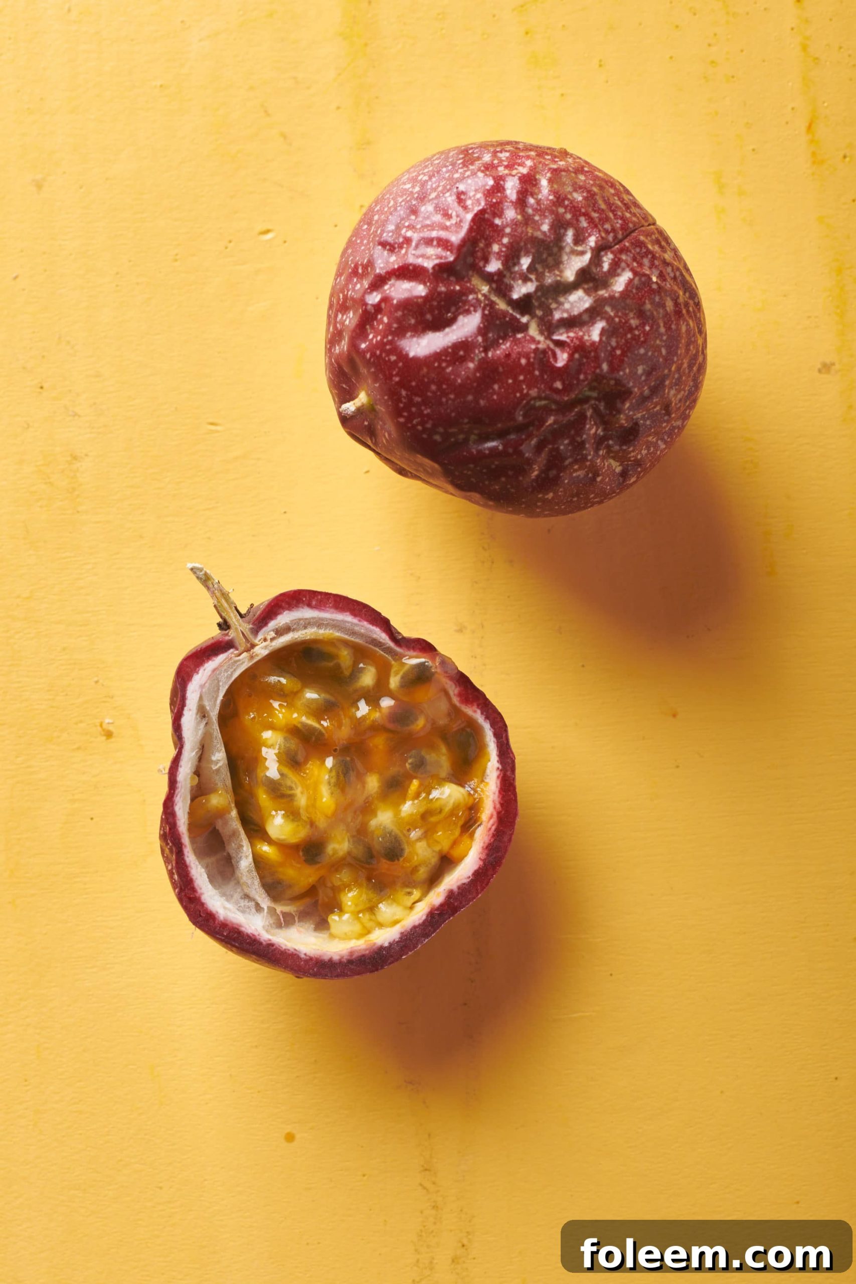 Two ripe passion fruits on a yellow surface.