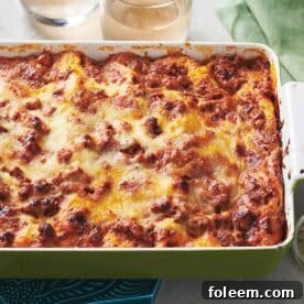 Classic meat lasagna in green and white baking dish on table.
