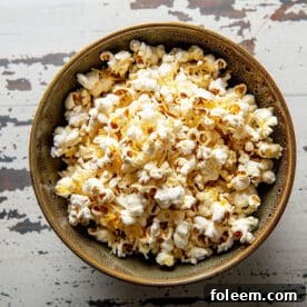 Homemade stovetop popcorn with cheddar cheese in bowl on wood table.