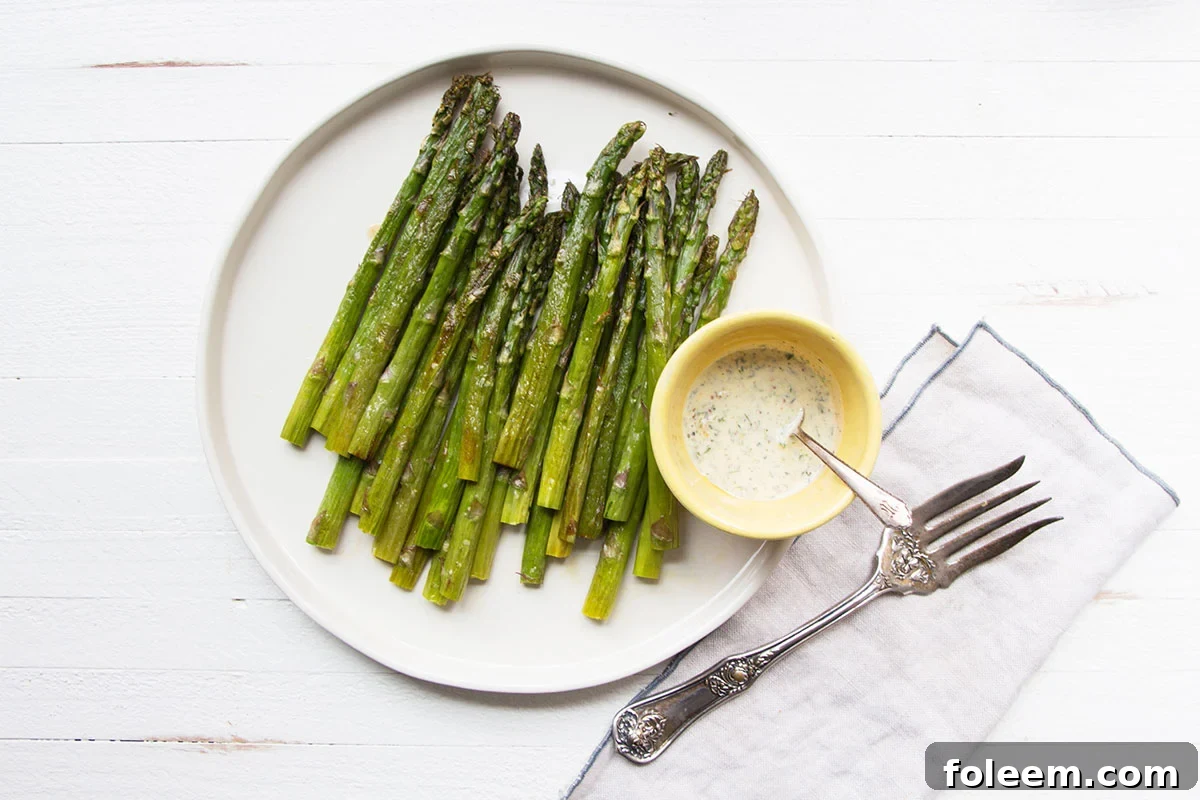 Roasted Asparagus on a plate with a bowl of Creamy Mustard-Oregano Sauce.