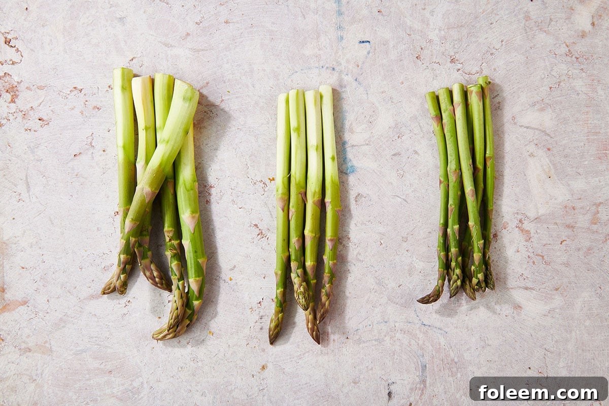 Thick, medium, and thin fresh asparagus spears on table.