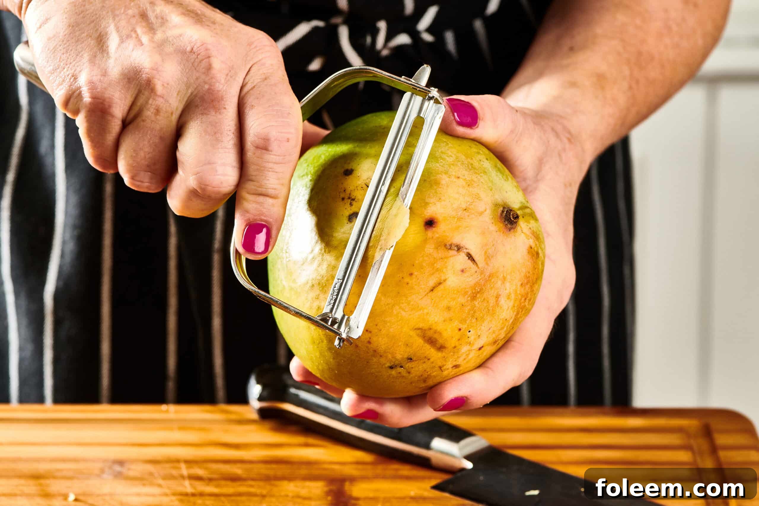 Woman using a peeler to peel a mango.