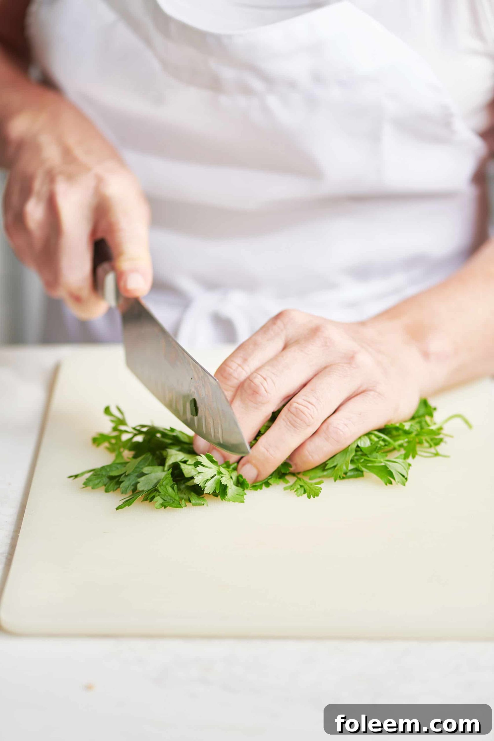 Chopping parsley on cutting board with chef knife.