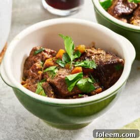 Beef stew in green bowls with parsley garnish.