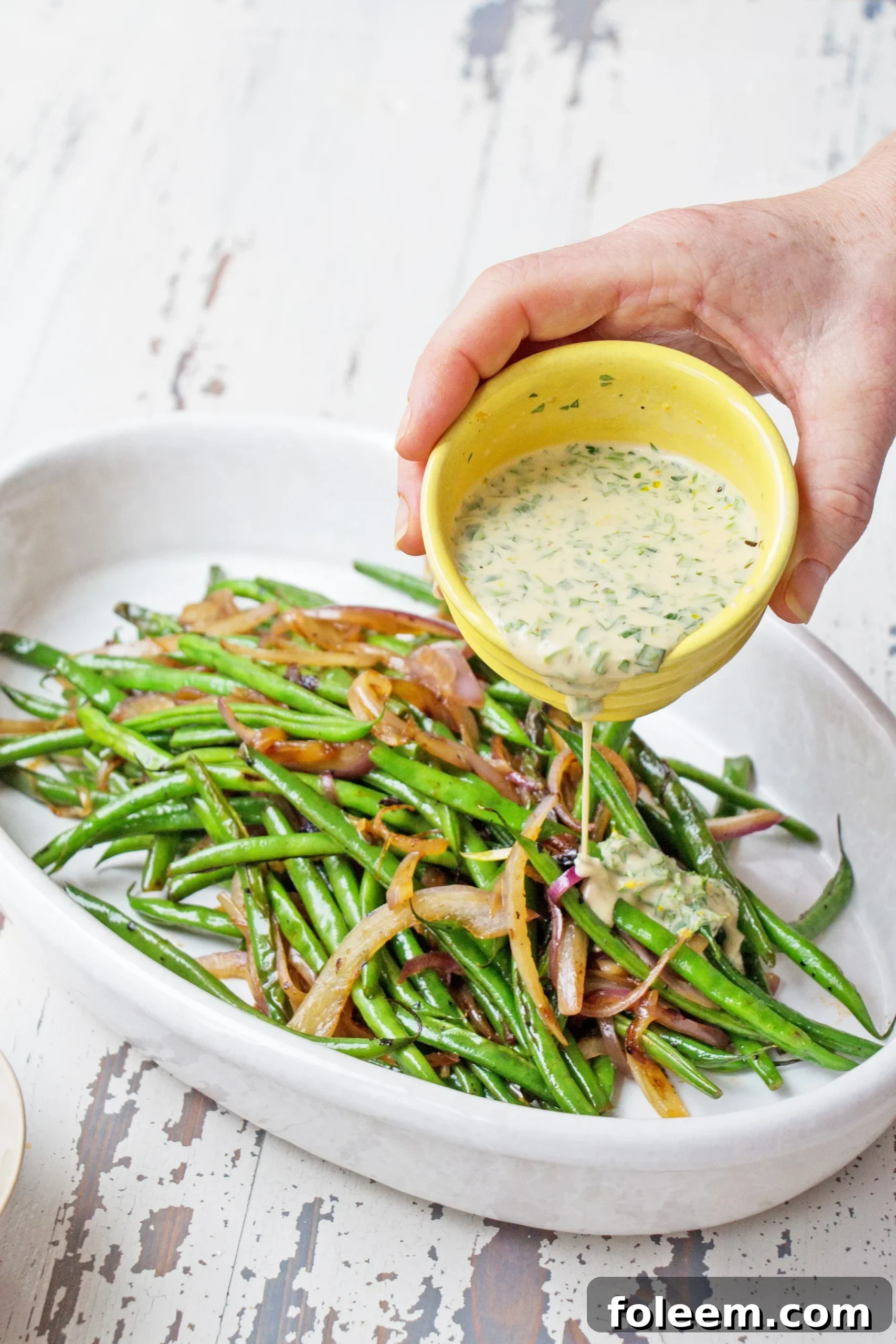 Pouring dressing over haricots verts and red onions.