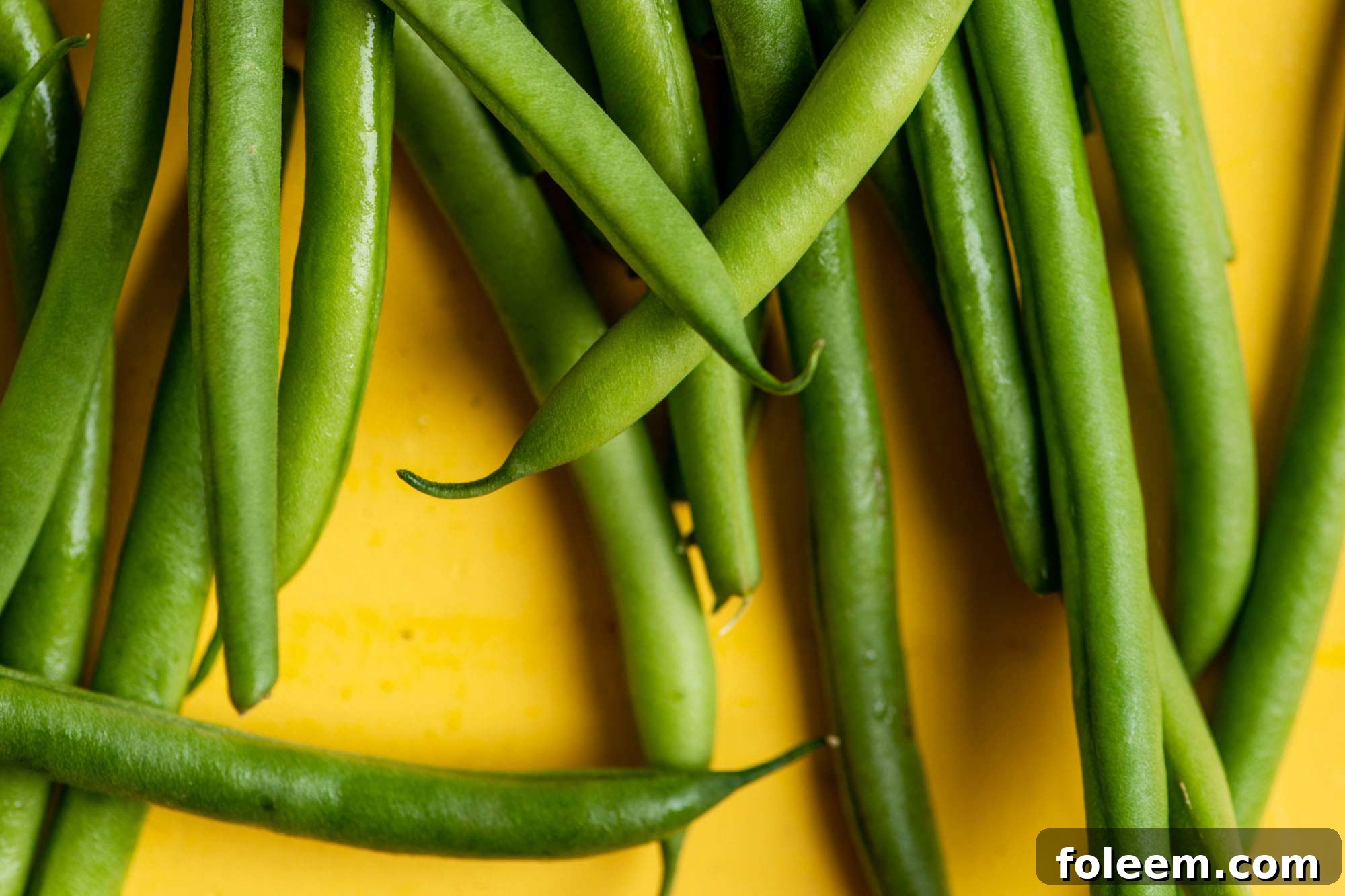 Whole Haricot Verts on a yellow surface.
