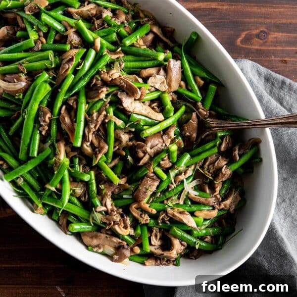 Sautéed green beans and mushrooms in serving dish with spoon.
